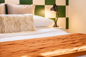 Un lit avec une tête de lit en bois, une literie blanche et un mur à carreaux verts et blancs.