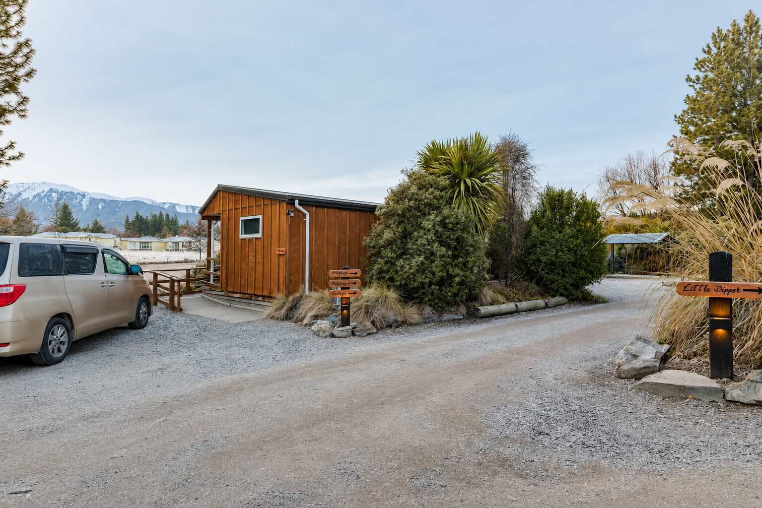 A gravel driveway leading to a wooden cabin with a van parked nearby.