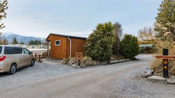 A gravel driveway leading to a wooden cabin with a van parked nearby.