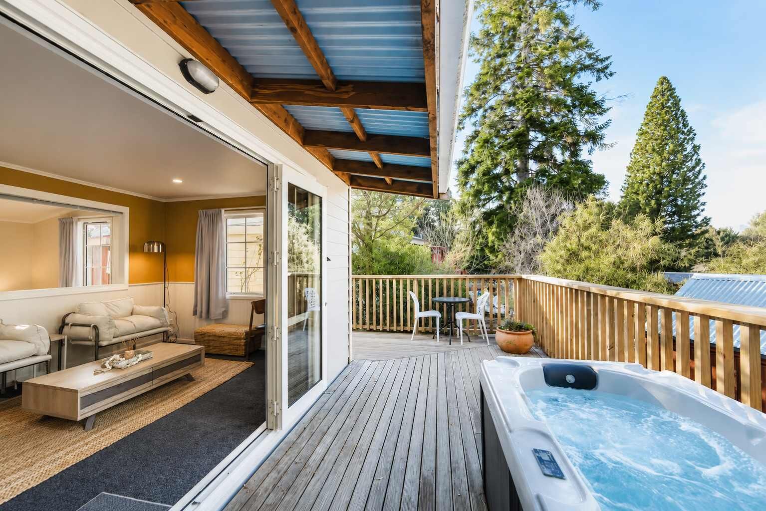 A deck with a hot tub, outdoor seating, and a view of trees.