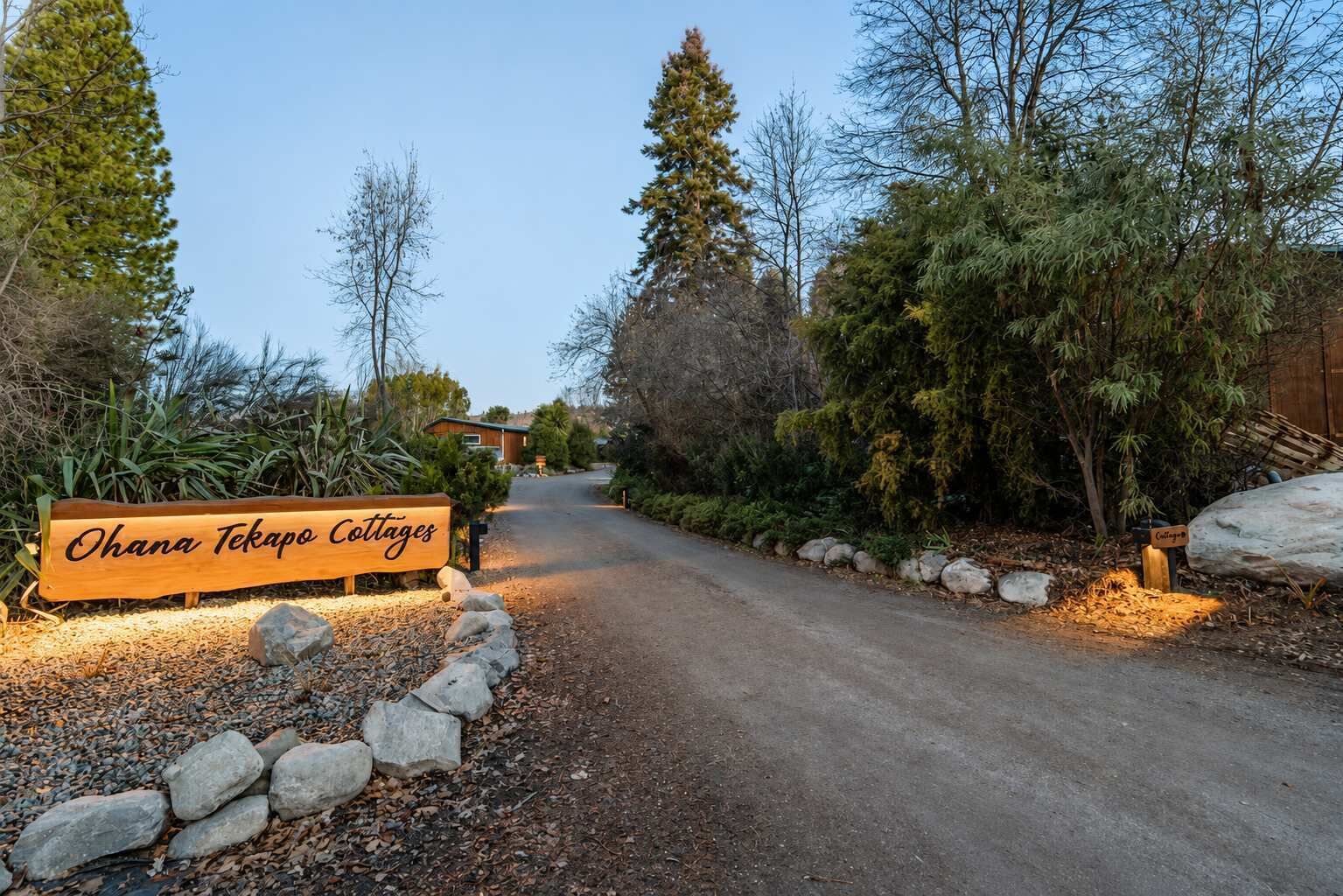 Ein Schild für die Ohana Tekapo Cottages, mit einem Kiesweg, der zu einem Gebäude führt.