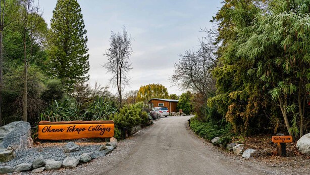 A gravel driveway leading to a wooden building with a sign reading 'Ohana Tekapo Cottages.' - Milkyway Lodge | Hot Tub + Scenic Views (Lake Tekapo)