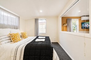A hotel room with a bed, curtains, a window, and a flat-screen TV.