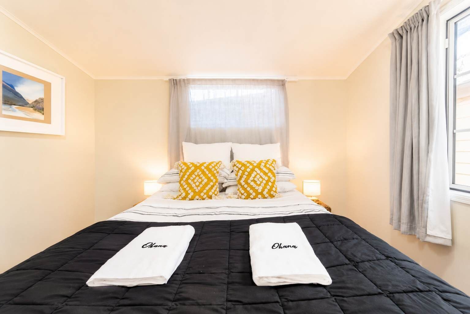 Ein Hotelzimmer mit einem Bett, zwei Kissen, einem Nachttisch mit Lampe und einem fenster mit Vorhängen.