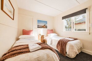 A hotel room with two beds, a nightstand, a window with a view, and a painting on the wall. - Little Dipper | 2BR | Near Lake + Church (Lake Tekapo)