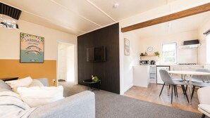 A modern living room with a sofa, a dining area with a table and chairs, a kitchen with a stove and microwave, and a TV mounted on the wall. - Little Dipper | 2BR | Near Lake + Church (Lake Tekapo)
