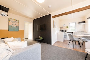 A modern living room with a sofa, a dining area with a table and chairs, a kitchen with a stove and microwave, and a TV mounted on the wall.