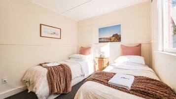 Habitación de hotel con dos camas, una mesita de noche, un ventanal y dos cuadros en la pared.