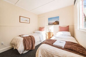 A hotel room with two beds, a nightstand, a window, and two framed pictures on the wall. - Little Dipper | 2BR | Near Lake + Church (Lake Tekapo)