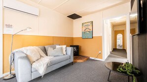 A living room with a sofa, a small table with a plant, a lamp, and a poster on the wall. - Little Dipper | 2BR | Near Lake + Church (Lake Tekapo)
