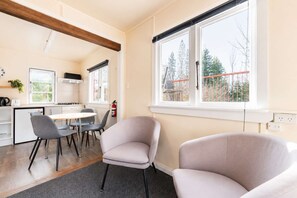 A modern kitchen with a dining area, a window with a view of trees, and a fire extinguisher on the wall. - Little Dipper | 2BR | Near Lake + Church (Lake Tekapo)