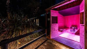 Eine Holzsauna mit Bank und Tisch, umgeben von Holzpflanzung und Vegetation.