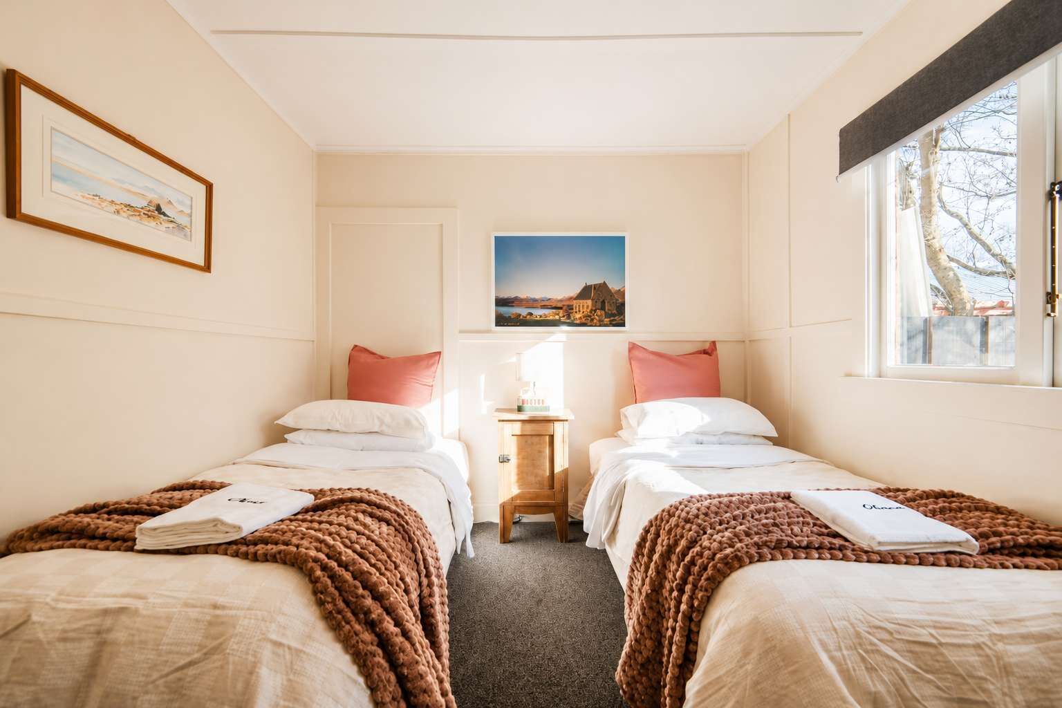 Une chambre d’hôtel avec deux lits, une table de chevet, un tableau encadré et une fenêtre.