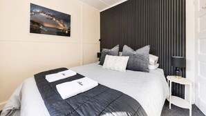 A hotel room with a bed, a nightstand, a lamp, a wall-mounted picture, and a dark headboard. - Little Dipper | 2BR | Near Lake + Church (Lake Tekapo)