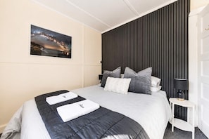 A hotel room with a bed, a nightstand, a lamp, a wall-mounted picture, and a dark headboard.