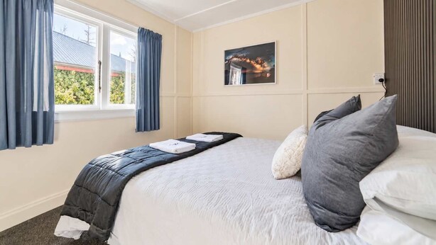 A hotel room with a bed, a window with curtains, a painting on the wall, and a view of the outside. - Little Dipper | 2BR | Near Lake + Church (Lake Tekapo)