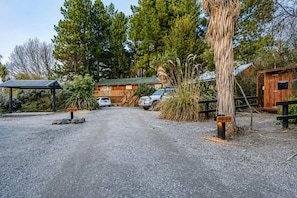 A gravel driveway leading to a wooden cabin with a metal roof, surrounded by tall trees and a small wooden structure. - Little Dipper | 2BR | Near Lake + Church (Lake Tekapo)