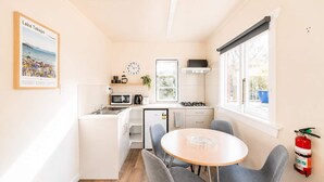 A compact kitchen with a dining area, a clock, and a fire extinguisher. - Little Dipper | 2BR | Near Lake + Church (Lake Tekapo)
