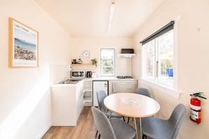 A compact kitchen with a dining area, a clock, and a fire extinguisher. - Little Dipper | 2BR | Near Lake + Church (Lake Tekapo)