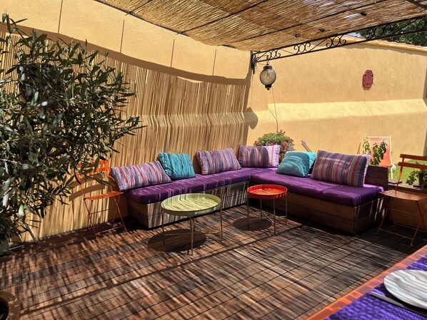 A cozy outdoor seating area with a cushioned sofa, a small round table, and a potted plant.