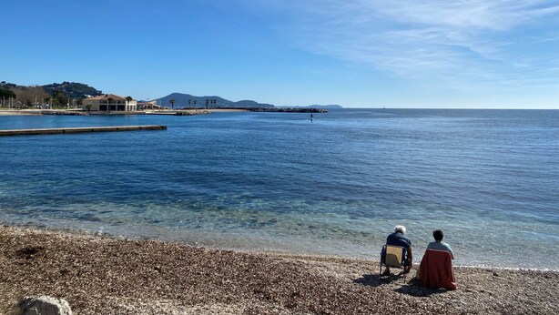 A pebbled beach with clear water, a distant lighthouse, and a mountain in the background. - Maison de Charme a Deux pas de la Méditerranée (Toulon)