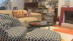 A living room with a sofa, ottoman, and a coffee table. There is a bookshelf filled with books and decorative items. A fireplace is visible in the background. - Maison de Charme a Deux pas de la Méditerranée (Toulon)