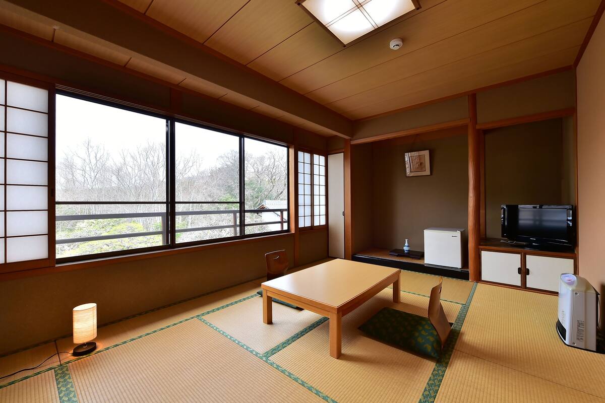 A traditional Japanese room with tatami flooring, a low table, a chair, a television, and a small refrigerator.