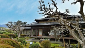En traditionel japansk bygning omgivet af omhyggeligt anlagte haver med forskellige træer og buske.