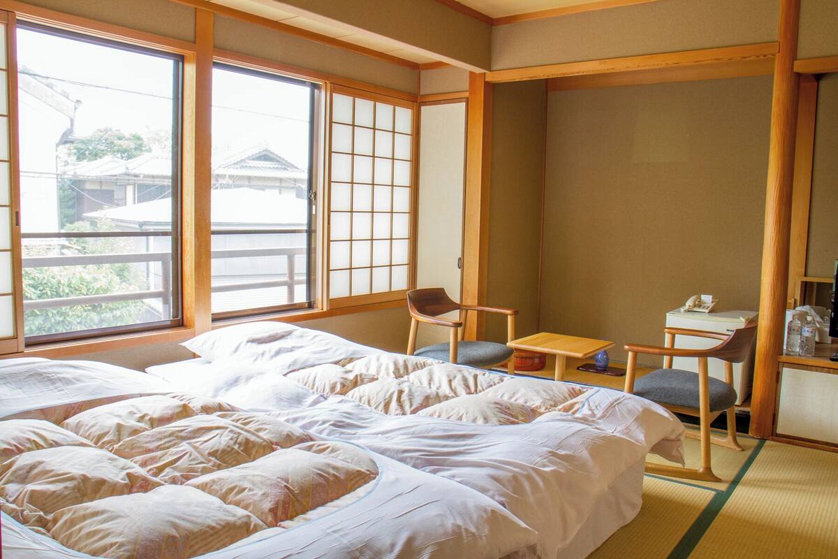 A traditional Japanese room with tatami flooring, a large bed, a desk with a chair, and a sliding shoji screen.