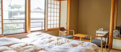 Una habitación japonesa tradicional con suelo de tatami, una cama grande, un escritorio con una silla y una puerta corredera shoji.