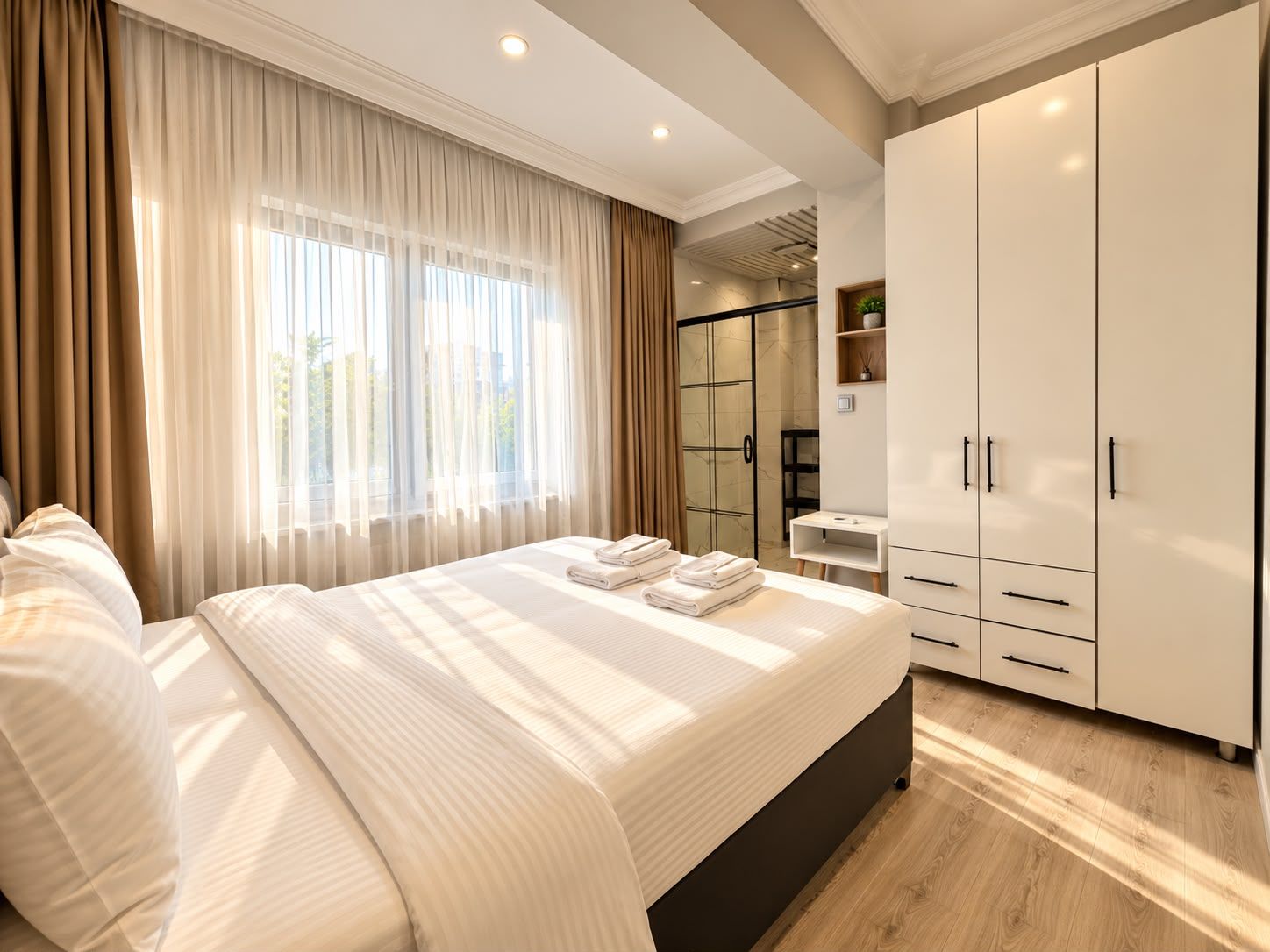 A modern hotel room with a large bed, a wardrobe, and a bathroom with a glass door.