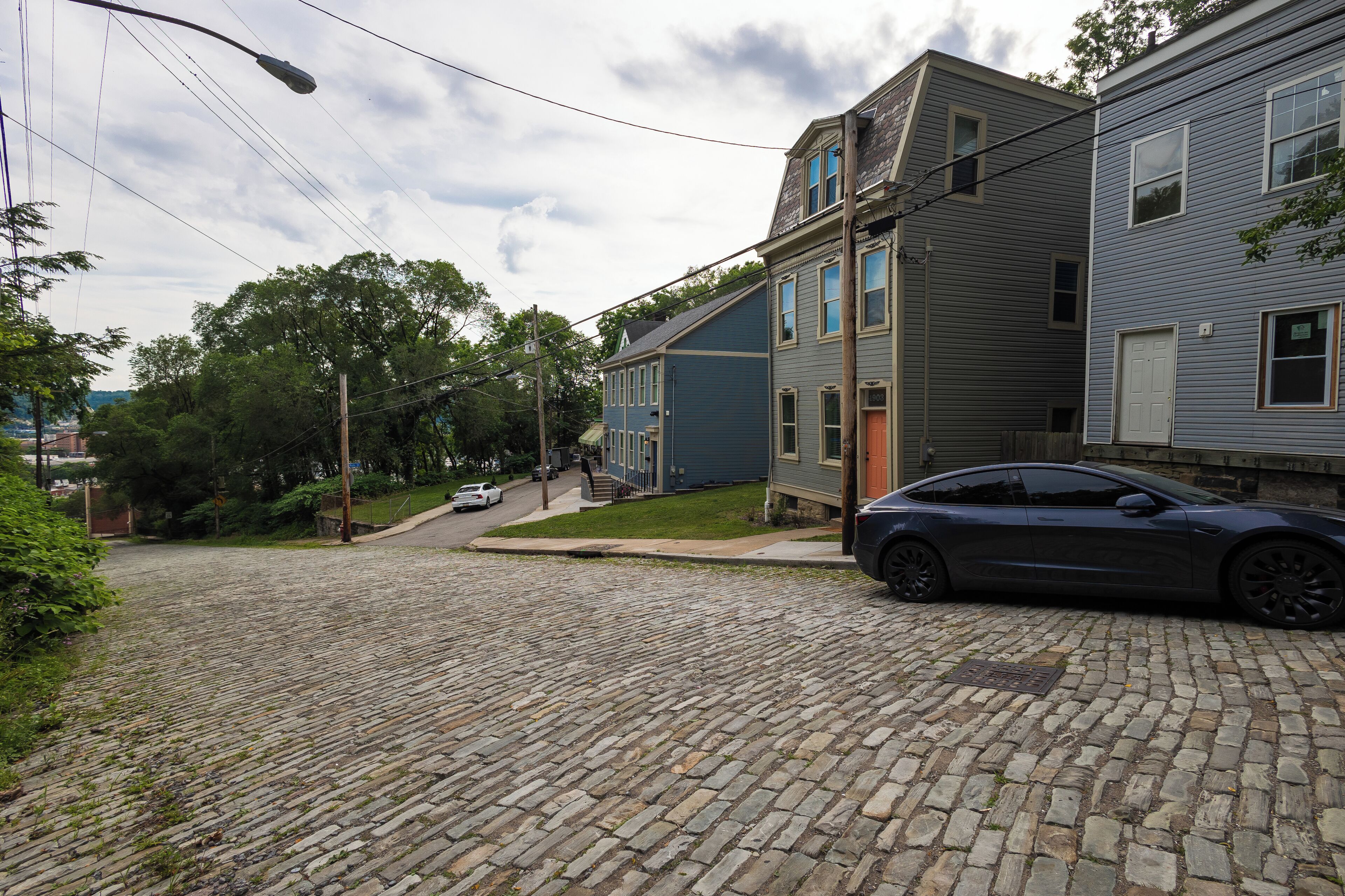 Une rue pavée dans un quartier résidentiel, avec des maisons, une voiture garée et un lampadaire.
