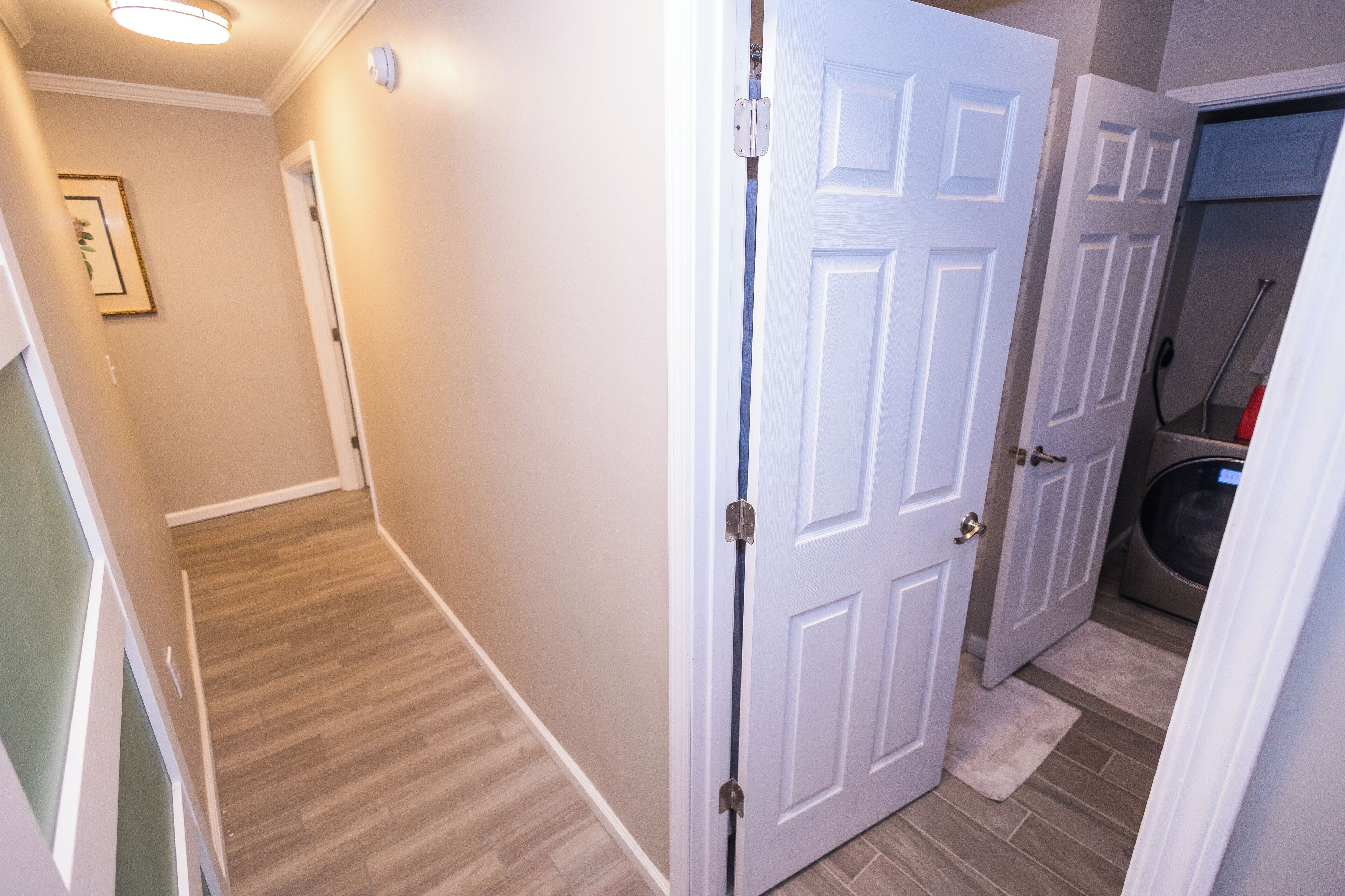 A hallway with a wooden floor, white walls, and a door leading to a laundry area.