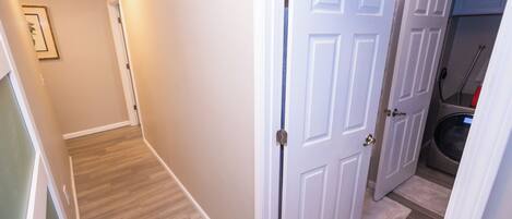 A hallway with a wooden floor, white walls, and a door leading to a laundry area.
