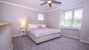 Quarto com cama, mesa de cabeceira, ventilador de teto e janela com persianas.