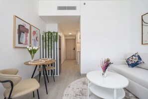 A modern living room with a white sofa, a round coffee table, and a dining area with a small round table and chairs. - Brand New & Modern Studio JVC (Dubai)