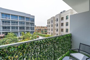 A balcony with a view of modern buildings, a green hedge, and a table with chairs. - Brand New & Modern Studio JVC (Dubai)