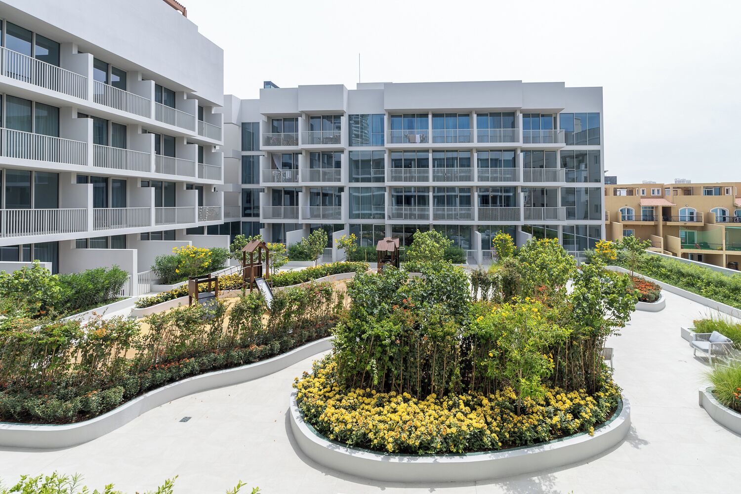 Un bâtiment moderne doté de nombreux balcons et d’un jardin sur le toit aménagé, avec diverses plantes et des espaces de détente.