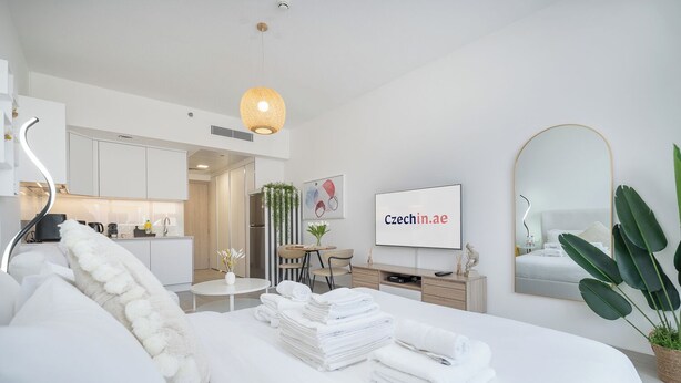 A modern hotel room with a neatly made bed, a dining area, a kitchen, and a large mirror. - Brand New & Modern Studio JVC (Dubai)