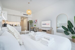 A modern hotel room with a neatly made bed, a dining area, a kitchen, and a large mirror. - Brand New & Modern Studio JVC (Dubai)
