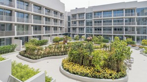 A modern multi-story building with balconies and a landscaped courtyard with plants and seating areas. - Brand New & Modern Studio JVC (Dubai)