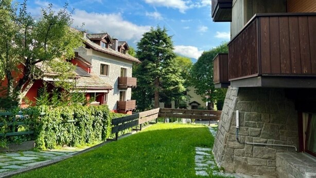 Un edificio residencial con fachada de piedra, terraza de madera y césped cuidado.