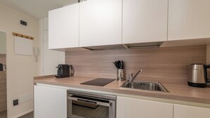 Una cocina moderna con armarios blancos, horno empotrado, lavabo y cafetera.