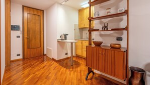Una cocina con armarios de madera, una encimera blanca y una estantería empotrada con objetos decorativos.