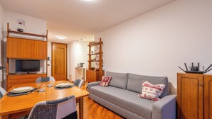 Un espacio habitable compacto con sofá, mesa de comedor y televisor sobre un mueble de madera.