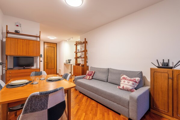 A compact living space with a sofa, dining table, and a TV on a wooden cabinet.