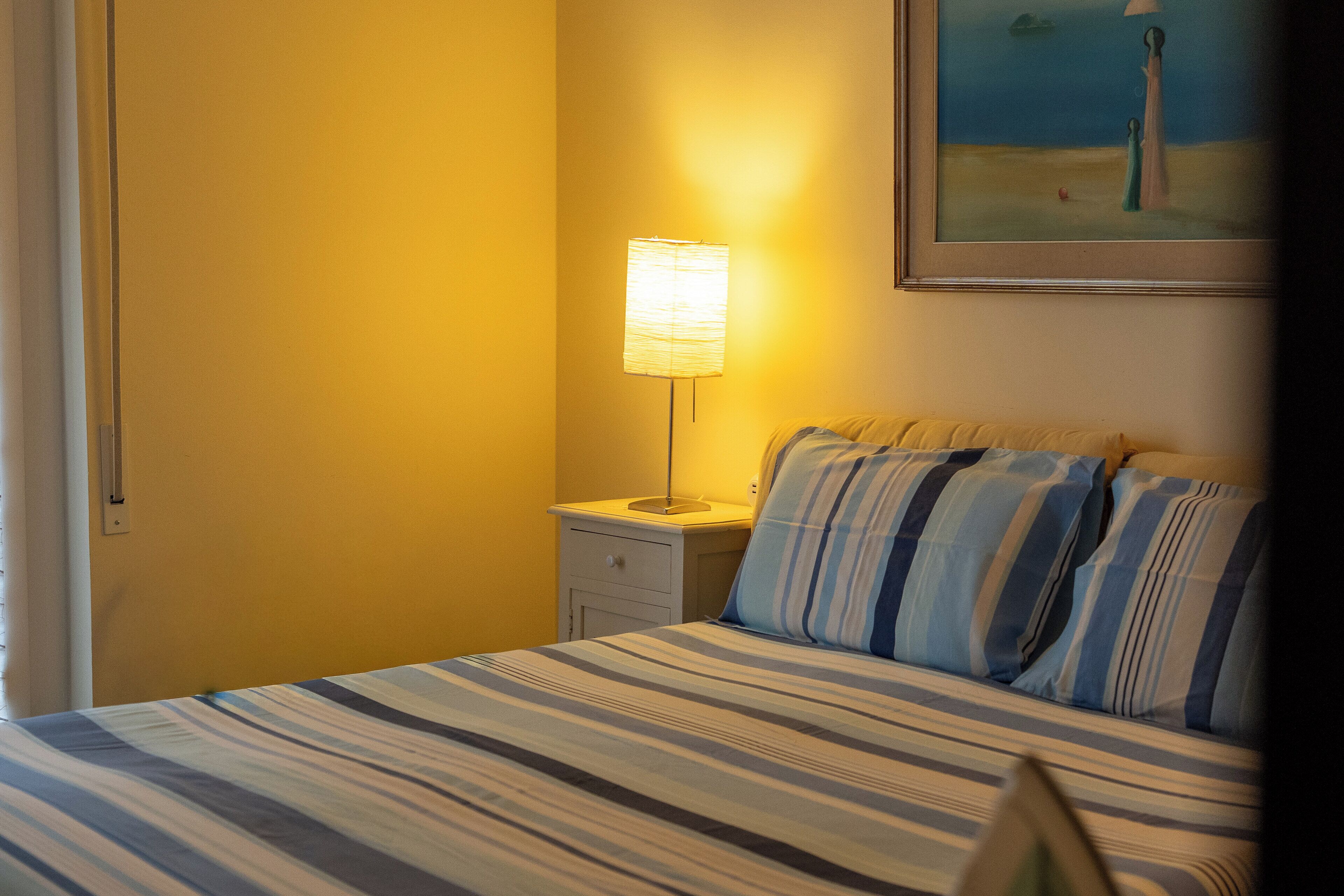 A hotel room with a bed, a nightstand, a lamp, and a painting on the wall.