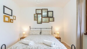 Un dormitorio ordenado con una cama, dos mesitas de noche con lámparas, y una pared decorada con cuadros.