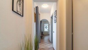 Un pasillo con una planta en maceta, una obra de arte enmarcada y una puerta que da a otra habitación.