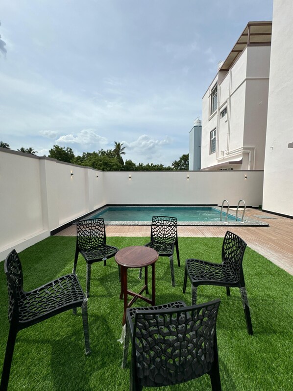 Une terrasse sur le toit avec une piscine, entourée de gazon synthétique et de chaises en métal.